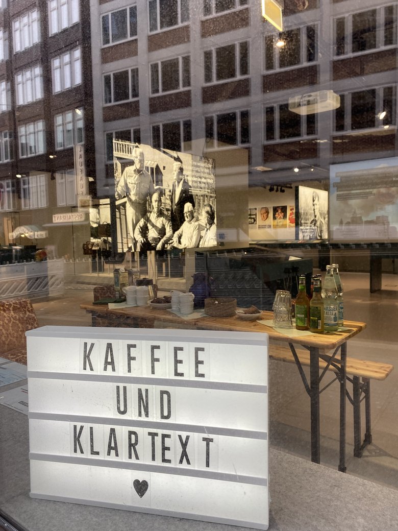 A coffee bar with a bright sign that reads "Coffee and plain text". Behind it, historical photos.
