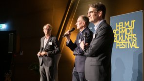 Colour photo: three people standing on a podium
