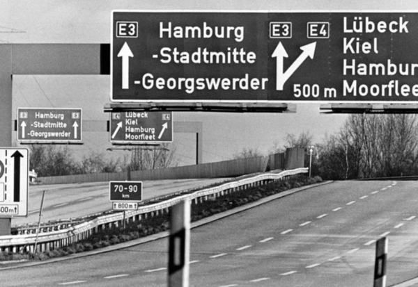 Schwarzweiß-Foto einer leeren Autobahn mit Autobahn-Schildern, die Richtung Hamburg führen.