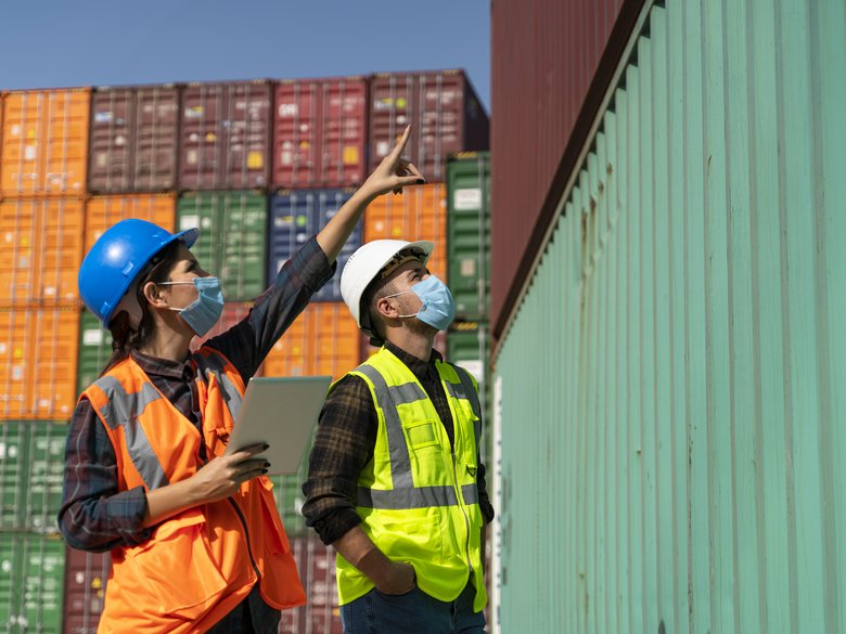 Workers with helmets and high-visibility waistcoats in front of harbour containers