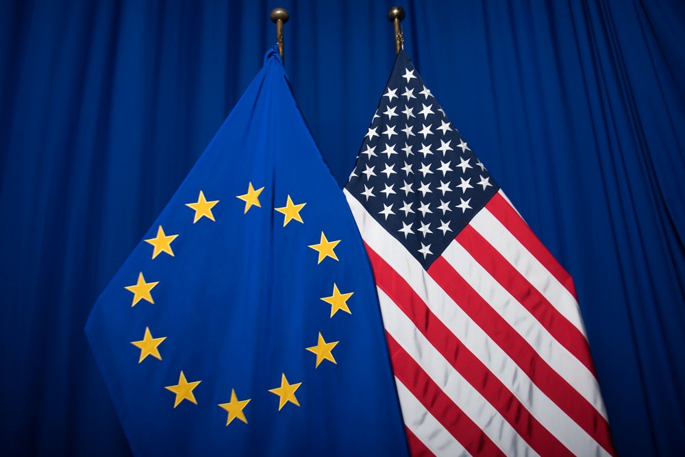 Die Euro-Flagge und die USA-Flagge vor einem blauen Vorghang