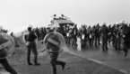 Black and white image of crowd of police officers in protective gear and with water cannon