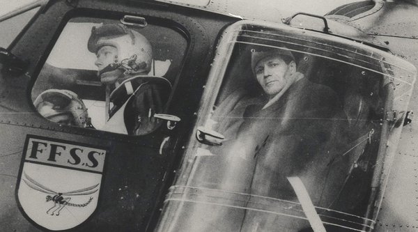 Helmut Schmidt schaut aus dem Fenster eines Hubschraubers, vor ihm sitzt ein Pilot.