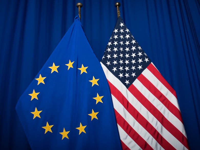 Die Euro-Flagge und die USA-Flagge vor einem blauen Vorghang