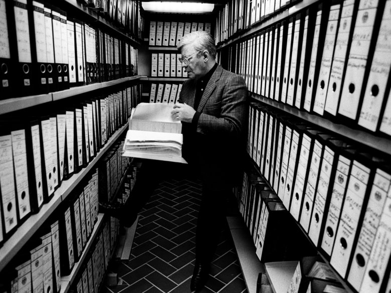 Helmut Schmidt with book in hand in archive with cupboards full of files