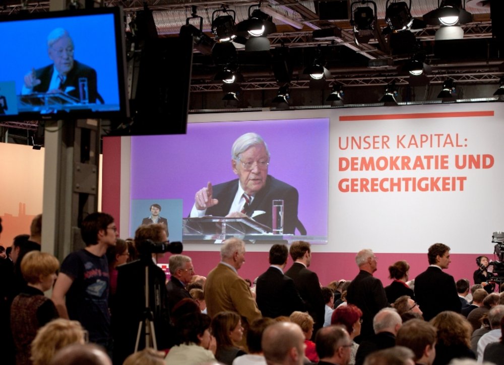 Helmut Schmidt gives a speech in 2011 and is projected onto the wall. An audience sits in front of him