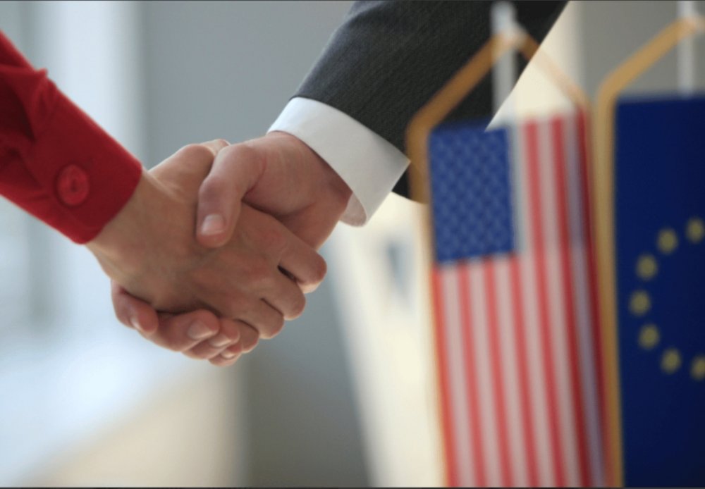 Handshake with USA and European flag in the foreground.