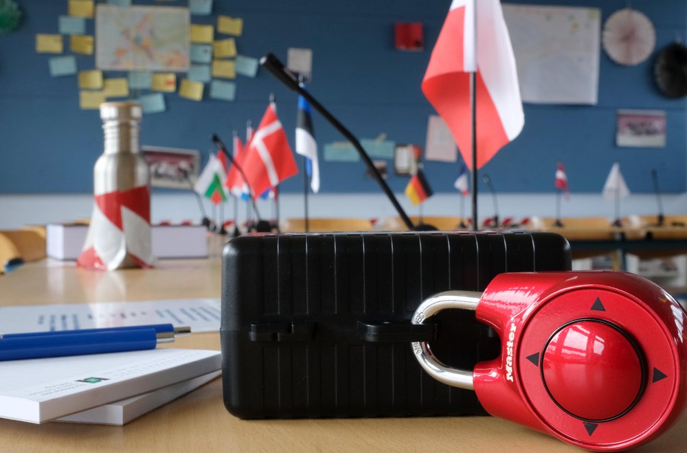 The escape game is shown during a break. EU flags are in the background and a castle is in the foreground.