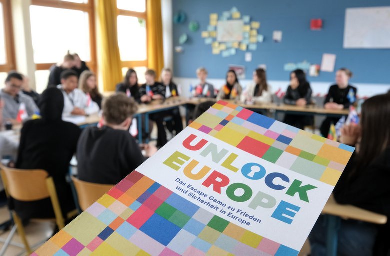 Colour photo: Flyer for the escape game Unlock Europe. In the background, young people are sitting at tables.