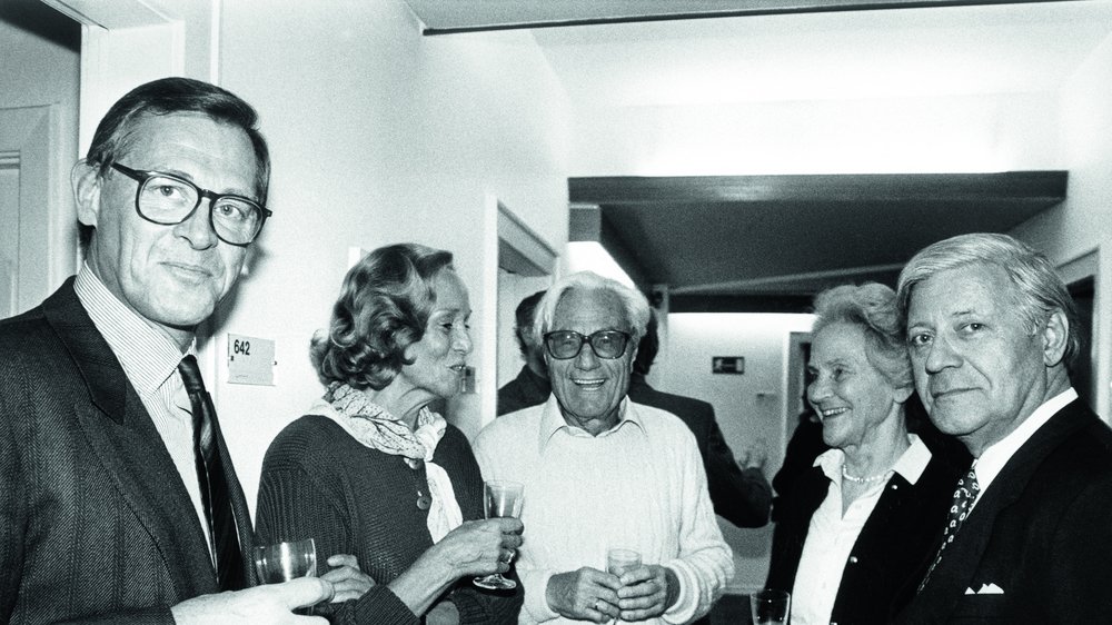 Schwarz-weiß Foto von drei Männern und zwei Frauen mit Sektgläsern in der Hand.
