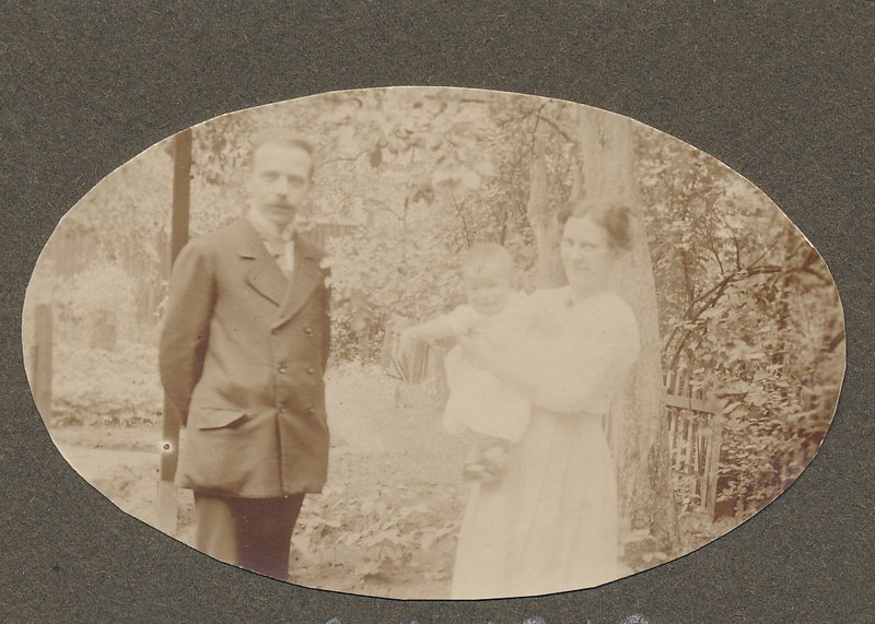 Historische Sepiaaufnahme 1919: Helmut Schmidt als Kleinkind im Arm seiner Mutter, daneben sein Vater im Anzug; aufgenommen im Freien vor Bäumen und einem Gartenzaun.