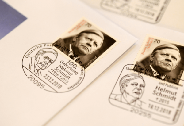Großaufnahme einer Briefmarke mit einem Schwarz-Weiß-Porträt Schmidts und ein Stempelabdruck, der die Gesichtszüge von Helmut Schmidt abbildet.