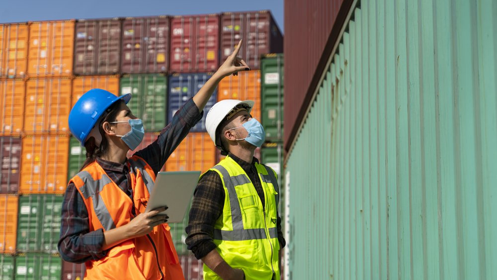 People in high-visibility waistcoats and helmets in front of containers