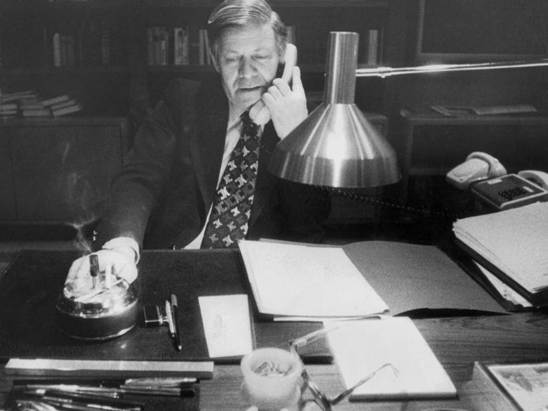 Helmut Schmidt at his office desk with a telephone receiver to his ear.