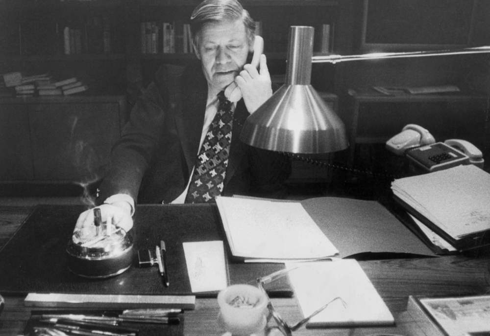 Helmut Schmidt at his office desk with a telephone receiver to his ear.