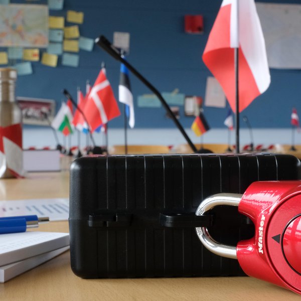 Colour photo: The setup for the escape game. A locked suitcase on a table, with flags of European countries in the background