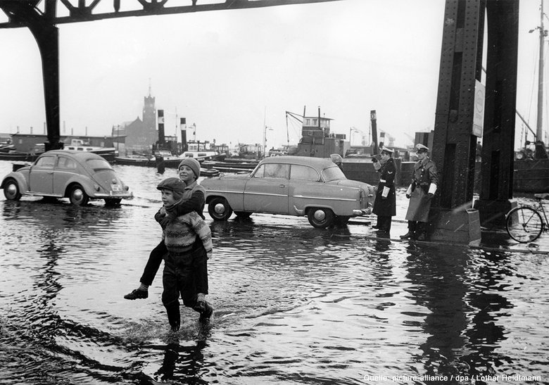 Überschwemmtes Stadtgebiet, Menschen und Autos stehen im Wasser