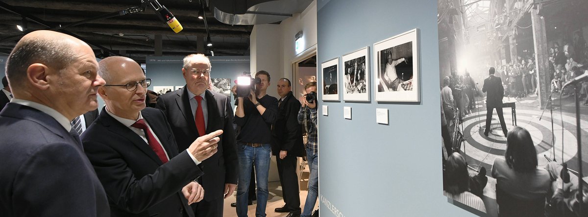 Olaf Scholz, Peter Tschentscher und Peer Steinbrück sehen Fotografien in der Ausstellung an. Die Situation wird von einem Kamera-Team begleitet.