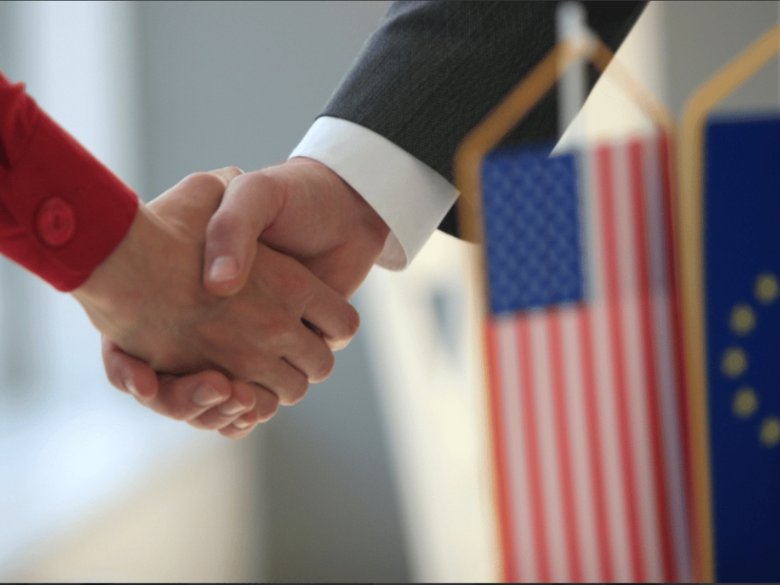 Handshake with USA and European flag in the foreground.