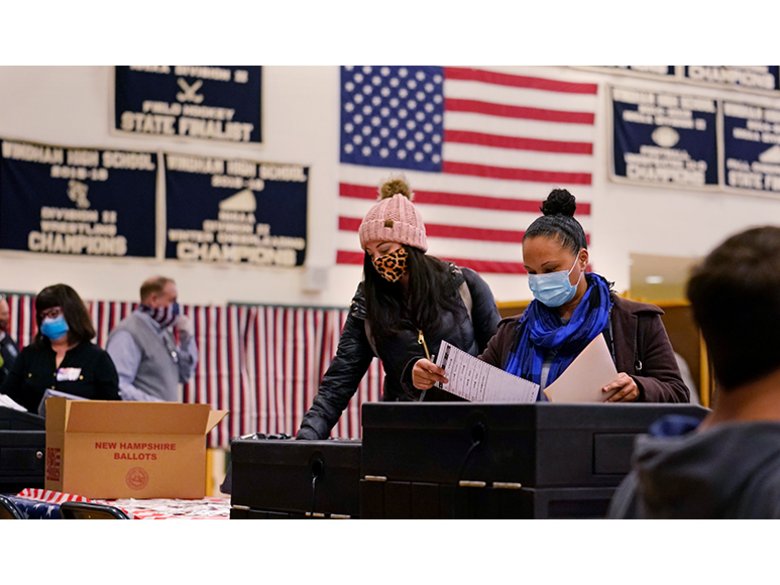 Wahllokal in Amerika, Personen mit Atemschutzmasken stehen an Wahlurnen