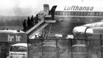 Black and white photograph of people walking up the gangway to an Lufthansa aircraft