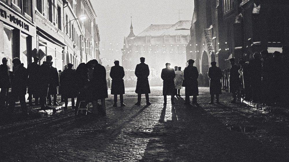 Black and white shot of a row of people in a street from behind