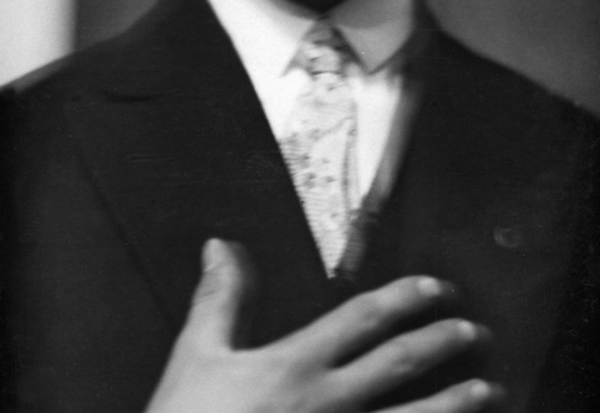 Unscharfe Schwarz-Weiß-Fotografie von einem singenden Mann. Seine Hand liegt auf der Brust, der obere Teil des Gesichts ist durch den Bildrand abgeschnitten.. 