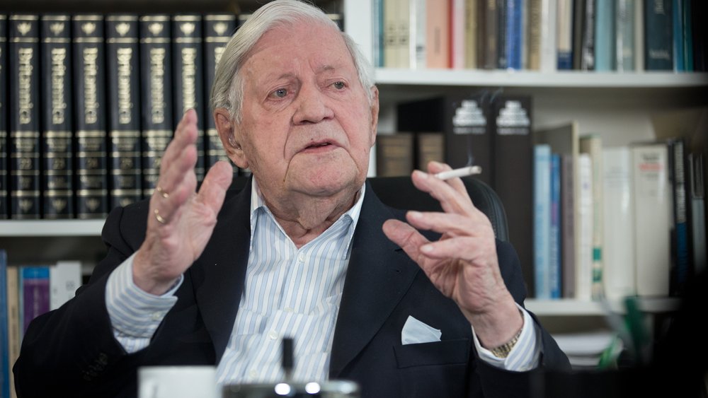 Farbfoto: Helmut Schmidt in seinem Büro vor Bücherregalen, erklärt etwas mit erhobenen Händen; eine Zigarette zwischen den Fingern.