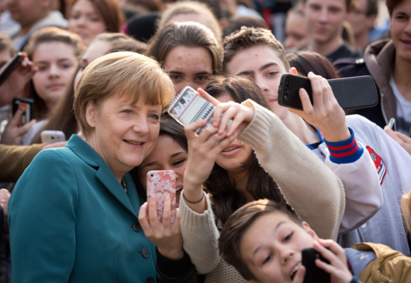 Angela Merkel ist von vielen jungen Menschen umgeben, die Handyfotos mit ihr aufnehmen.