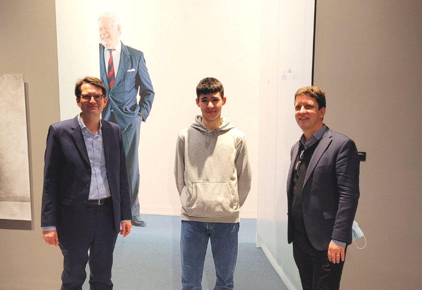 Die drei Personen stehen vor einem großen Foto vom Altkanzler Schmidt in der Ausstellung.