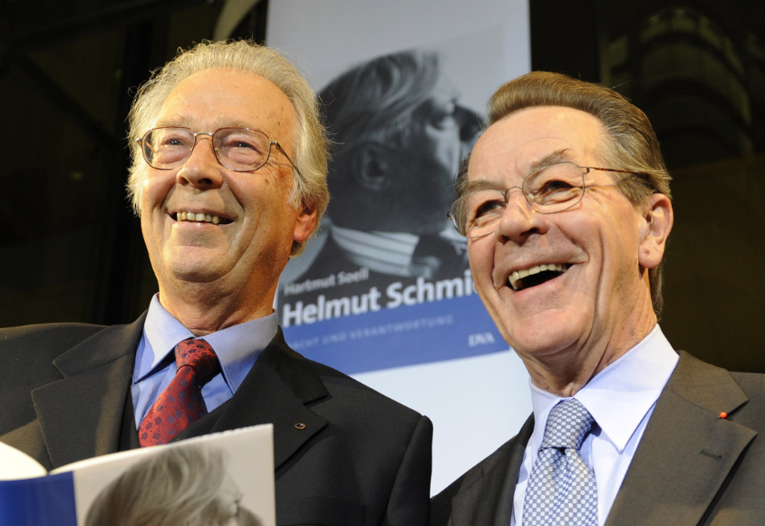 Zwei Männer blicken in den Raum. Hinter ihnen ist ein Plakat von Helmut Schmidt. 